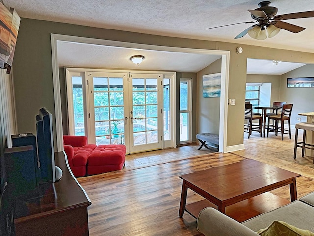 living room with a textured ceiling, lofted ceiling, ceiling fan, french doors, and light hardwood / wood-style floors