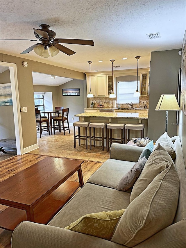 living room featuring ceiling fan, sink, a textured ceiling, and a wealth of natural light