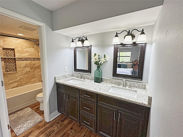 full bathroom featuring tiled shower / bath combo, toilet, dual bowl vanity, and hardwood / wood-style flooring