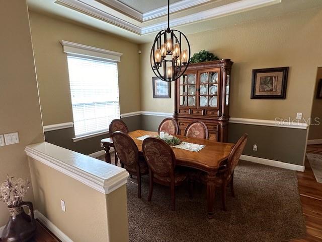 dining area featuring a notable chandelier, crown molding, a tray ceiling, and dark wood-type flooring