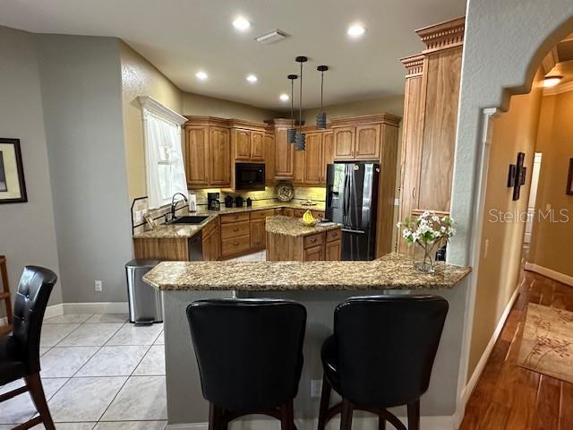 kitchen with light hardwood / wood-style flooring, kitchen peninsula, light stone countertops, stainless steel fridge, and sink