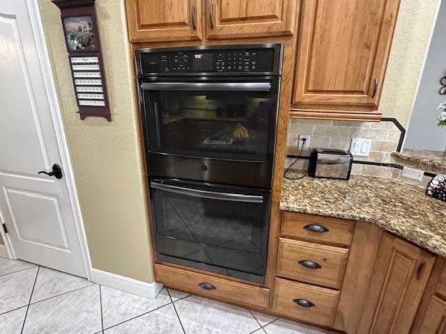 kitchen featuring backsplash, stone countertops, light tile patterned flooring, and black double oven