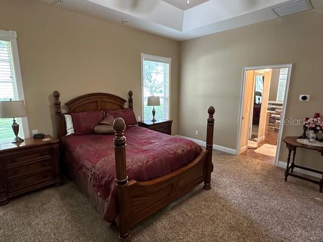 bedroom with a tray ceiling, light colored carpet, and ensuite bathroom