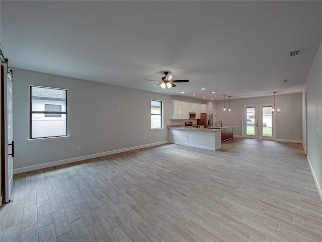 unfurnished living room with ceiling fan, a barn door, french doors, and light hardwood / wood-style floors