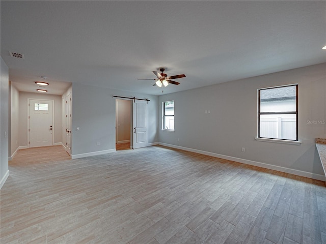 spare room with a barn door, ceiling fan, and light hardwood / wood-style floors