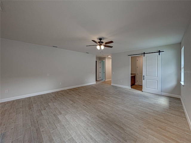 spare room featuring ceiling fan, a barn door, and light hardwood / wood-style flooring