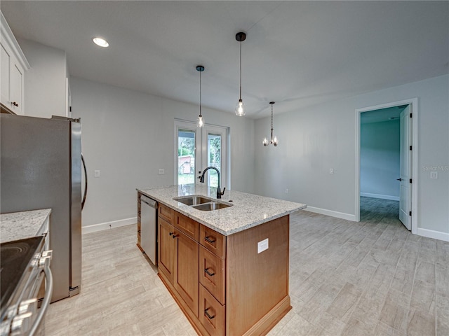 kitchen featuring light wood-type flooring, stainless steel appliances, an island with sink, light stone countertops, and sink