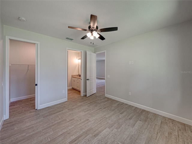 unfurnished bedroom with light hardwood / wood-style flooring, ceiling fan, a spacious closet, connected bathroom, and a closet