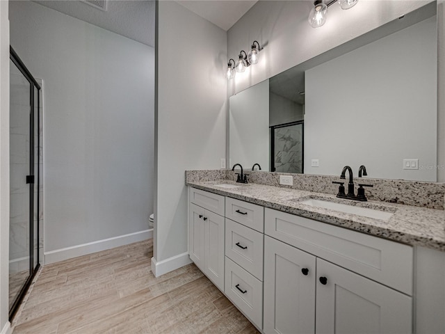 bathroom featuring double sink vanity, a shower with shower door, hardwood / wood-style flooring, and toilet