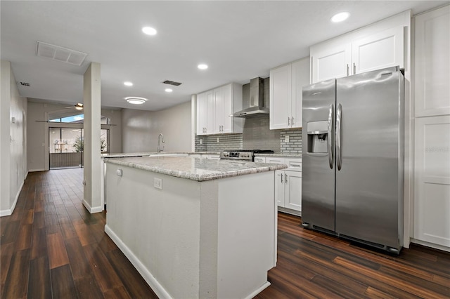 kitchen with wall chimney exhaust hood, dark wood-type flooring, stainless steel appliances, light stone counters, and white cabinets