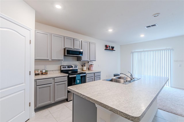 kitchen with appliances with stainless steel finishes, a center island with sink, gray cabinets, and sink