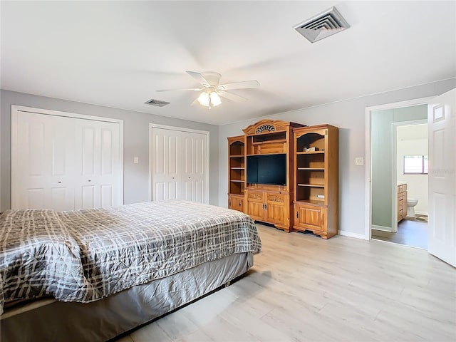 bedroom with light wood-type flooring, two closets, visible vents, and baseboards