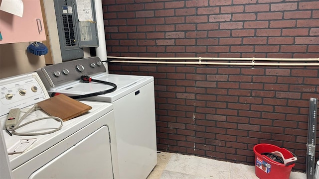 clothes washing area featuring cabinets, brick wall, washer and dryer, and electric panel