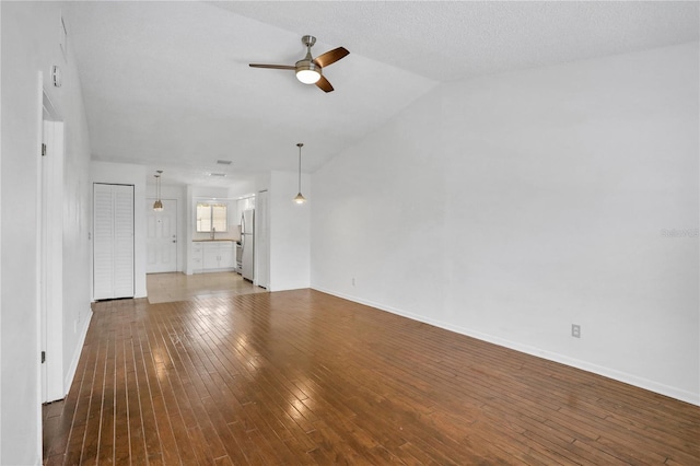 unfurnished living room featuring ceiling fan, a textured ceiling, hardwood / wood-style floors, and vaulted ceiling