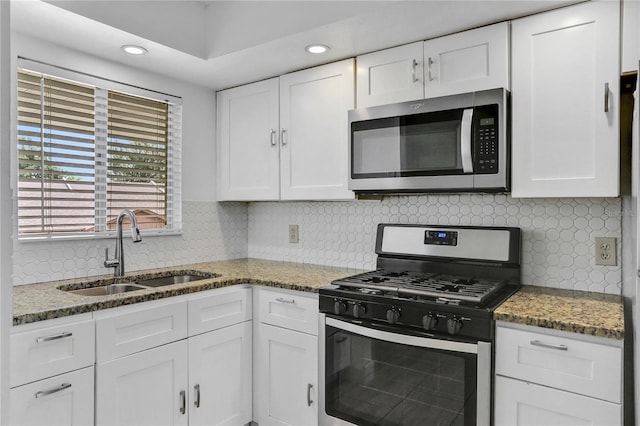 kitchen featuring stainless steel appliances, white cabinetry, a sink, and dark stone countertops