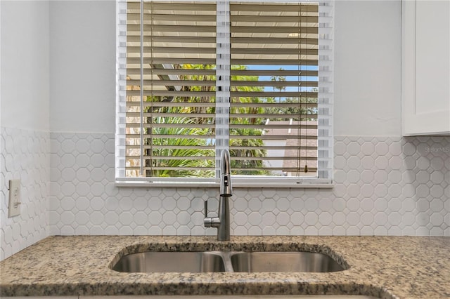 room details featuring stone countertops, a sink, white cabinets, and decorative backsplash