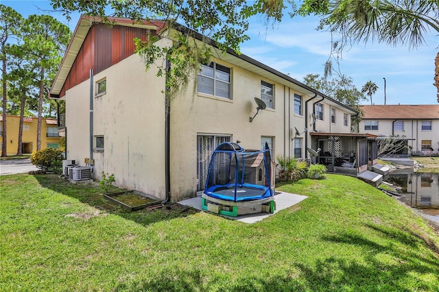 back of property featuring stucco siding, a trampoline, and a yard