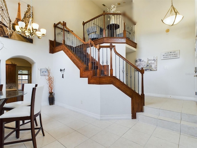 staircase featuring a towering ceiling, tile patterned flooring, and an inviting chandelier