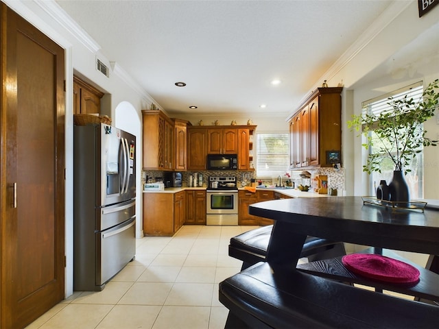 kitchen with appliances with stainless steel finishes, crown molding, tasteful backsplash, and light tile patterned floors