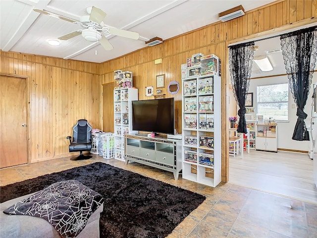 living room featuring ceiling fan, light tile patterned floors, wooden walls, and beamed ceiling