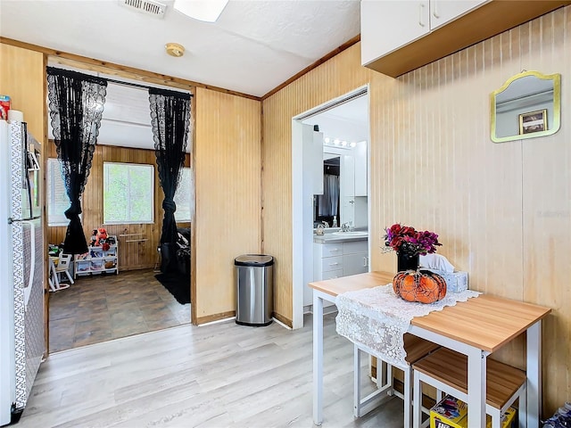 kitchen featuring sink, stainless steel fridge, light hardwood / wood-style floors, and wooden walls