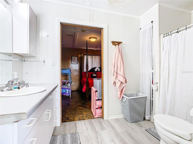 bathroom featuring toilet, wooden walls, vanity, hardwood / wood-style floors, and ornamental molding