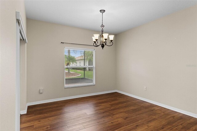 spare room featuring an inviting chandelier and dark hardwood / wood-style flooring