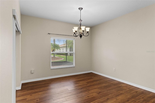 spare room with baseboards, an inviting chandelier, and wood finished floors