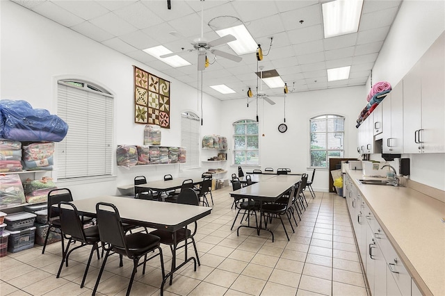 dining space featuring a ceiling fan, a skylight, light tile patterned floors, a paneled ceiling, and a towering ceiling