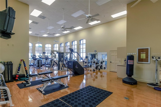 exercise room with wood finished floors, a ceiling fan, baseboards, radiator heating unit, and a towering ceiling
