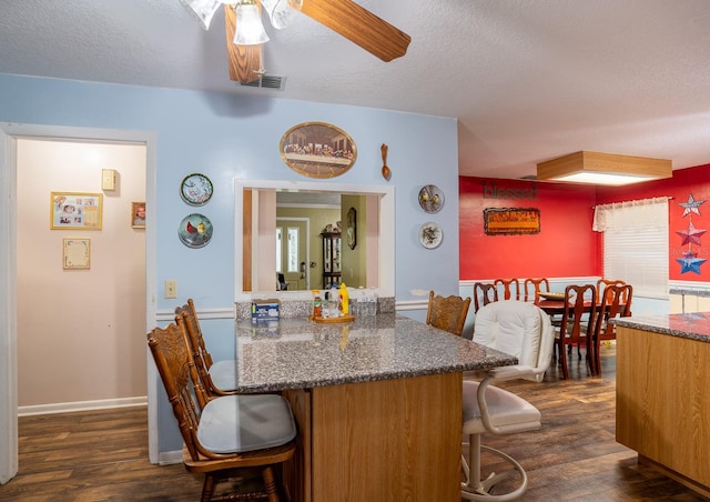 kitchen featuring a textured ceiling, a ceiling fan, a kitchen breakfast bar, and dark wood-style flooring