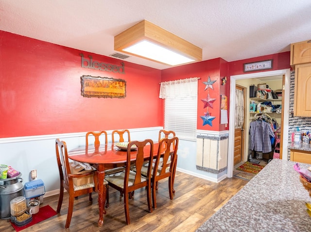 dining room with a wainscoted wall, visible vents, a textured ceiling, and wood finished floors