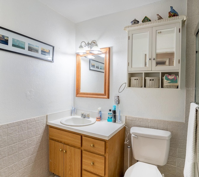 bathroom featuring toilet, a wainscoted wall, tile walls, and vanity