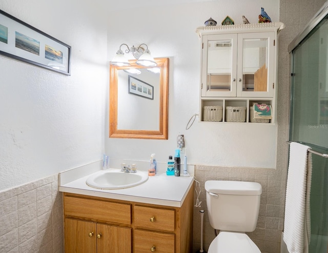 full bathroom featuring toilet, a shower with shower door, a wainscoted wall, vanity, and tile walls