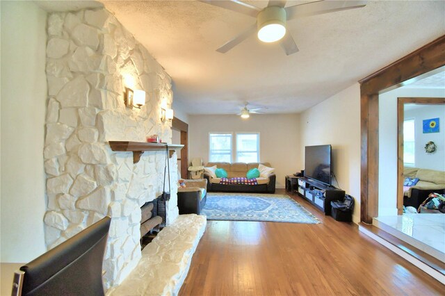 living room featuring hardwood / wood-style flooring, a fireplace, a textured ceiling, and ceiling fan