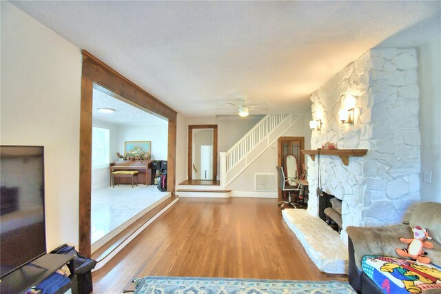 living room featuring a fireplace, ceiling fan, a textured ceiling, and wood-type flooring