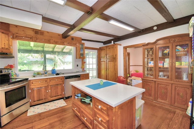 kitchen with appliances with stainless steel finishes, hardwood / wood-style floors, sink, beamed ceiling, and a kitchen island