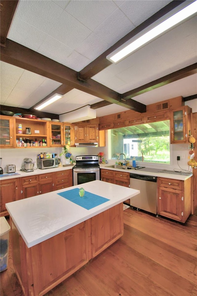 kitchen featuring beam ceiling, appliances with stainless steel finishes, light hardwood / wood-style floors, extractor fan, and a center island