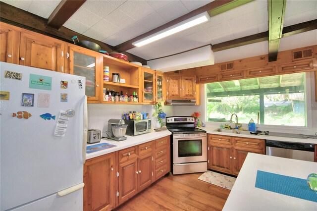 kitchen featuring sink, beamed ceiling, appliances with stainless steel finishes, and light hardwood / wood-style floors