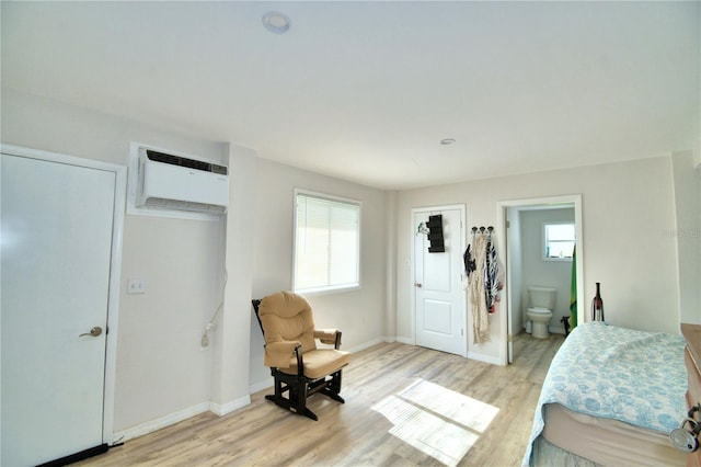 bedroom with a wall mounted AC, light wood-type flooring, and ensuite bath