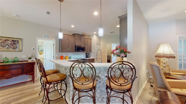 kitchen with a breakfast bar, hanging light fixtures, backsplash, and light hardwood / wood-style floors