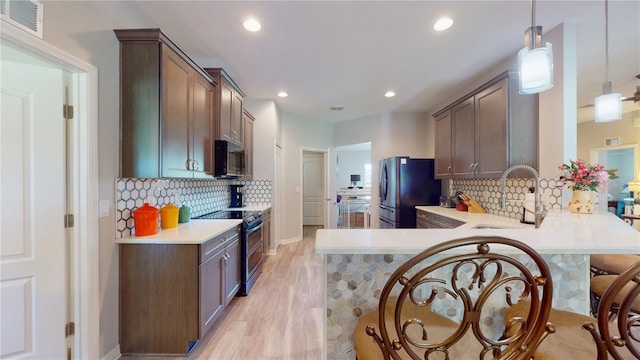 kitchen featuring hanging light fixtures, light hardwood / wood-style flooring, tasteful backsplash, kitchen peninsula, and black appliances