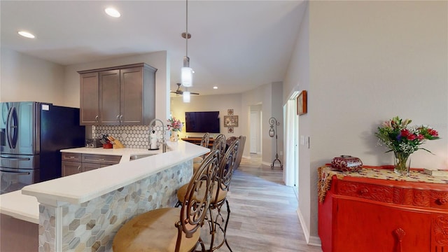 kitchen featuring a breakfast bar, backsplash, sink, light hardwood / wood-style flooring, and hanging light fixtures