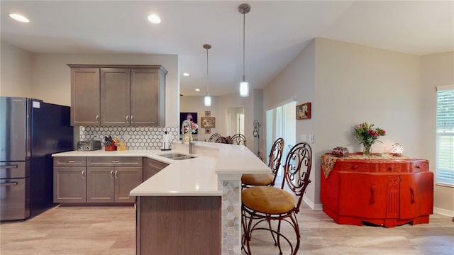 kitchen featuring backsplash, decorative light fixtures, light hardwood / wood-style floors, sink, and kitchen peninsula