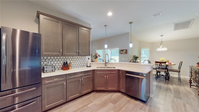 kitchen with pendant lighting, tasteful backsplash, light hardwood / wood-style floors, sink, and stainless steel appliances