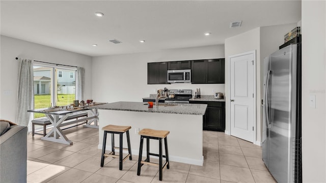 kitchen with stone counters, light tile patterned floors, stainless steel appliances, visible vents, and dark cabinets