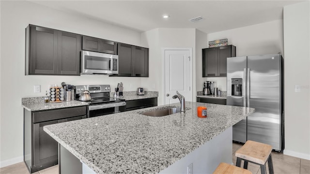 kitchen with a sink, visible vents, appliances with stainless steel finishes, light stone countertops, and a center island with sink