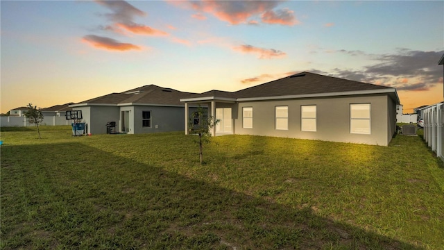 rear view of property featuring stucco siding, a lawn, central AC, and fence