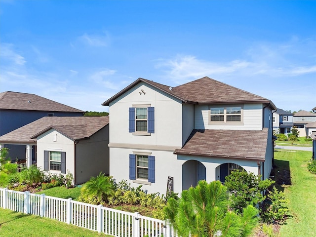 traditional home featuring a fenced front yard, roof with shingles, and stucco siding