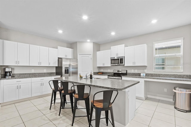 kitchen with a kitchen island with sink, sink, a breakfast bar, appliances with stainless steel finishes, and white cabinets